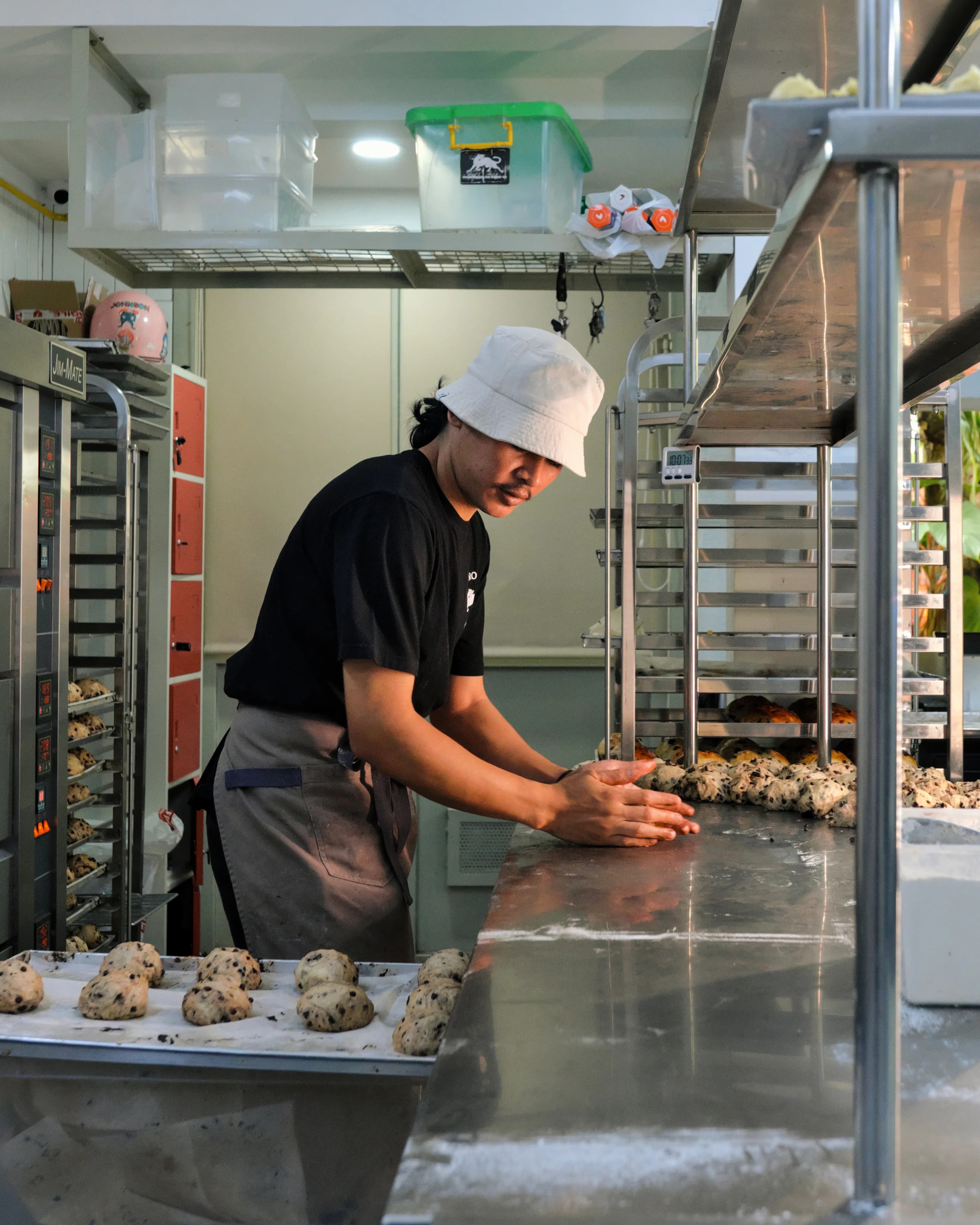 A baker in a roti macan apron shaping dough along the bench
