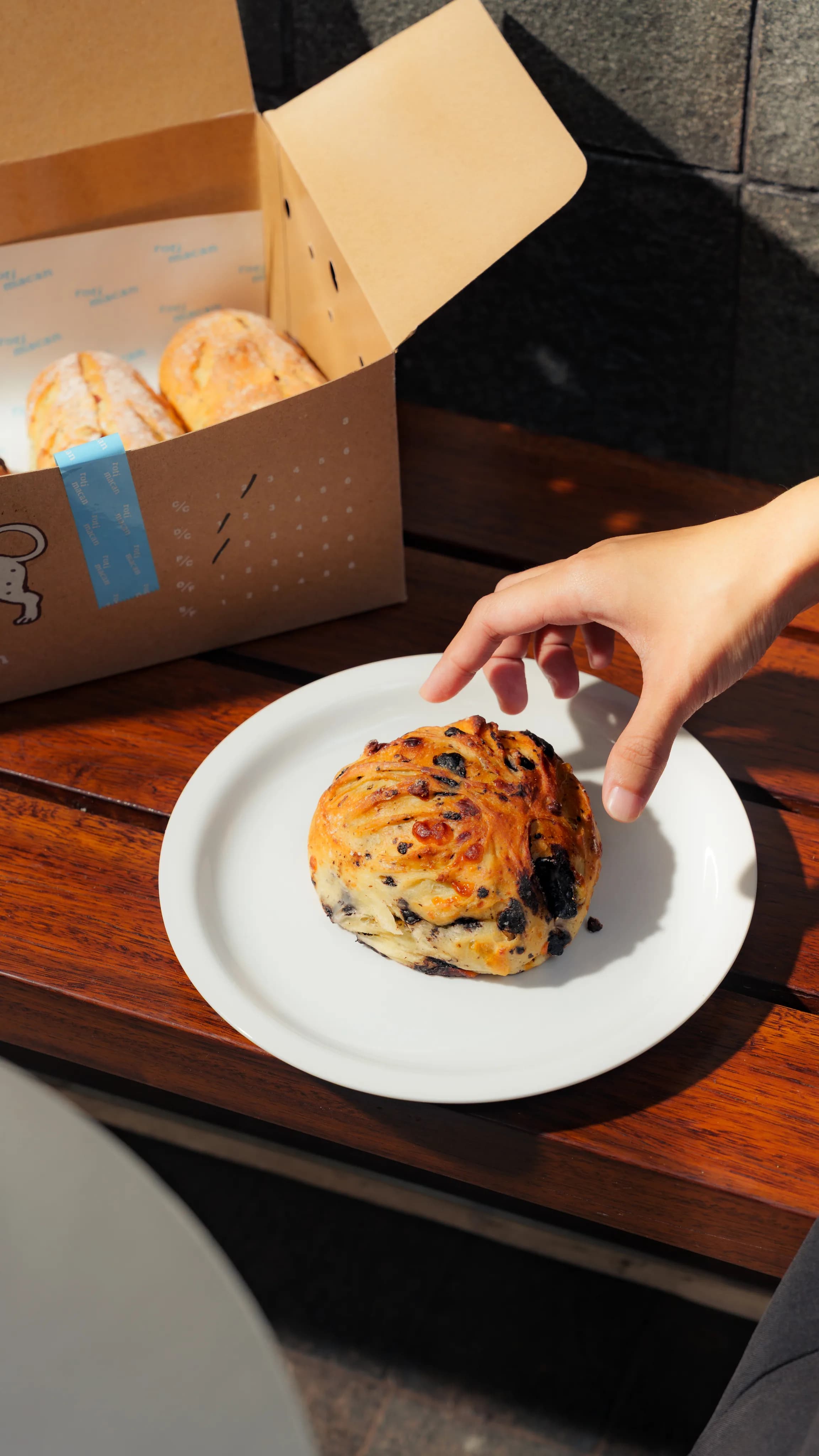 A hand reaching for a chocolate chip bun on a plate