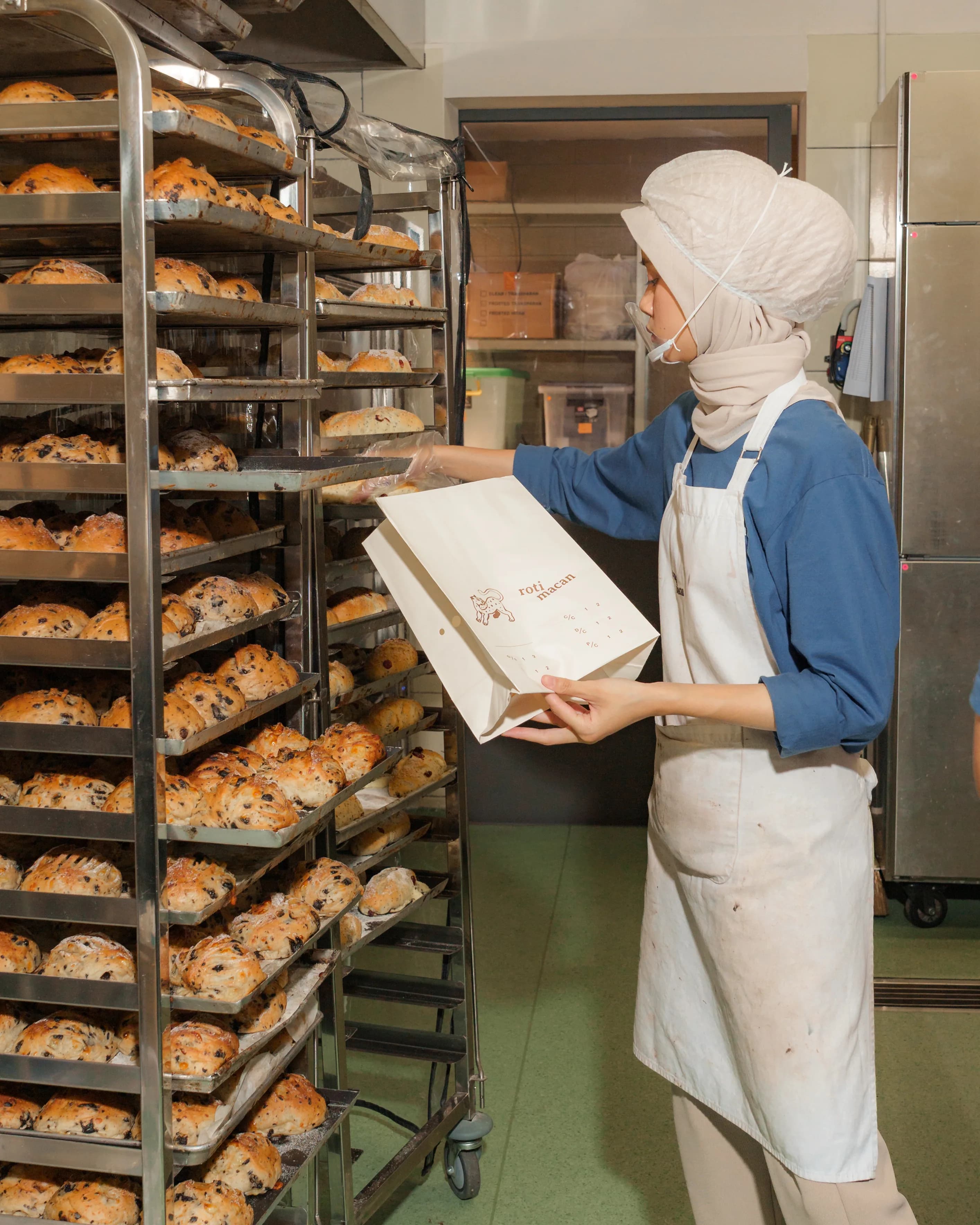 A baker bagging loaves in front of a rack stacked with the morning's bake